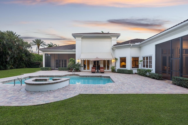 pool at dusk with an in ground hot tub, a patio, a lawn, and a sunroom