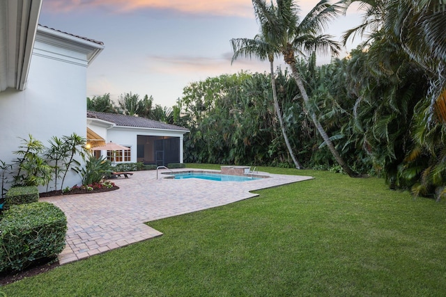 pool at dusk featuring a jacuzzi, a yard, and a patio area