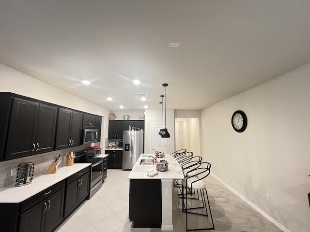 kitchen with a breakfast bar, backsplash, a kitchen island with sink, appliances with stainless steel finishes, and decorative light fixtures