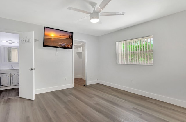 unfurnished bedroom with connected bathroom, ceiling fan, a spacious closet, wood-type flooring, and a closet