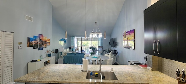 kitchen featuring high vaulted ceiling, light stone countertops, sink, and a chandelier