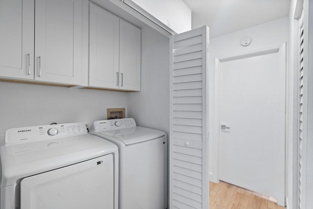 clothes washing area featuring cabinets, light hardwood / wood-style flooring, and washing machine and clothes dryer