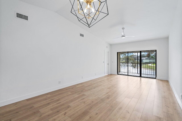 empty room with ceiling fan with notable chandelier, light hardwood / wood-style floors, and vaulted ceiling