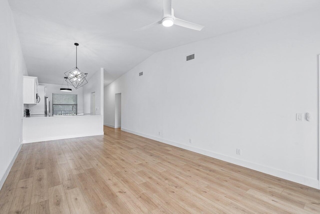 unfurnished living room featuring ceiling fan with notable chandelier, light hardwood / wood-style floors, and vaulted ceiling