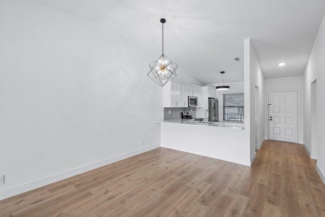 kitchen featuring kitchen peninsula, backsplash, stainless steel appliances, white cabinets, and lofted ceiling