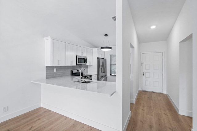 kitchen with kitchen peninsula, appliances with stainless steel finishes, pendant lighting, white cabinetry, and lofted ceiling