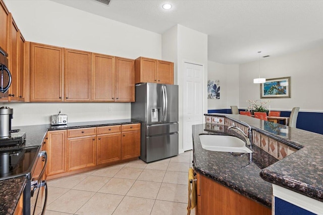 kitchen featuring stainless steel fridge, dark stone counters, sink, light tile patterned floors, and pendant lighting