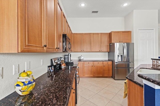 kitchen featuring dark stone counters, sink, light tile patterned floors, a textured ceiling, and appliances with stainless steel finishes