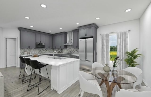 kitchen featuring light stone countertops, stainless steel appliances, wall chimney range hood, light hardwood / wood-style flooring, and decorative backsplash