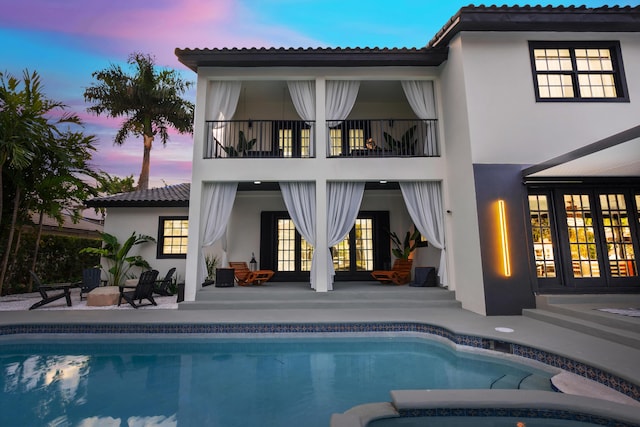 back house at dusk featuring a patio, a balcony, and french doors