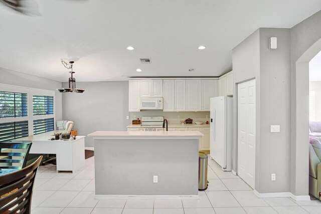 kitchen with white appliances, white cabinets, a center island with sink, hanging light fixtures, and light tile patterned flooring