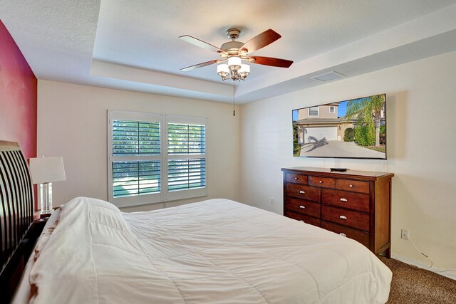 bedroom featuring a raised ceiling, ceiling fan, and carpet