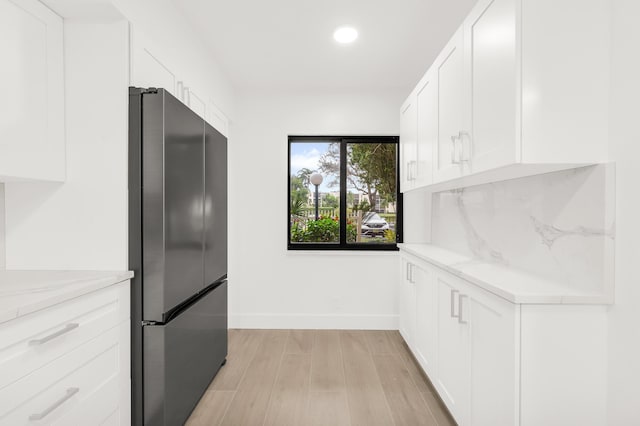 kitchen with white cabinets, light hardwood / wood-style floors, light stone counters, and stainless steel refrigerator