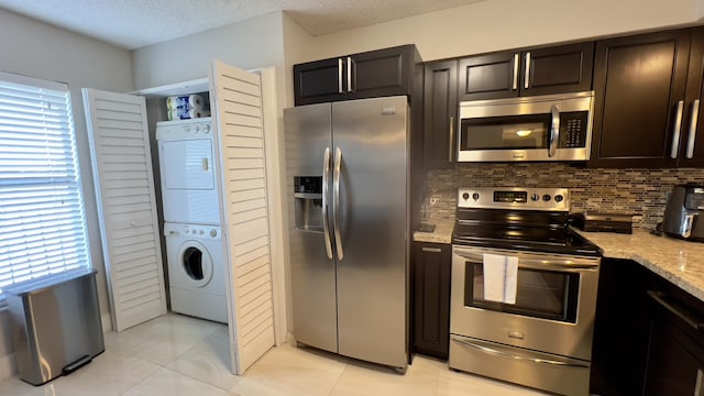 kitchen with stacked washing maching and dryer, stainless steel appliances, tasteful backsplash, light stone counters, and light tile patterned flooring