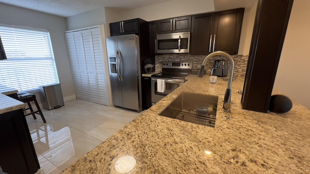 kitchen with a textured ceiling, appliances with stainless steel finishes, tasteful backsplash, light tile patterned flooring, and light stone counters