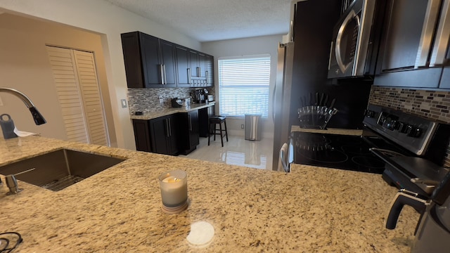 kitchen with light stone countertops, sink, backsplash, a textured ceiling, and appliances with stainless steel finishes