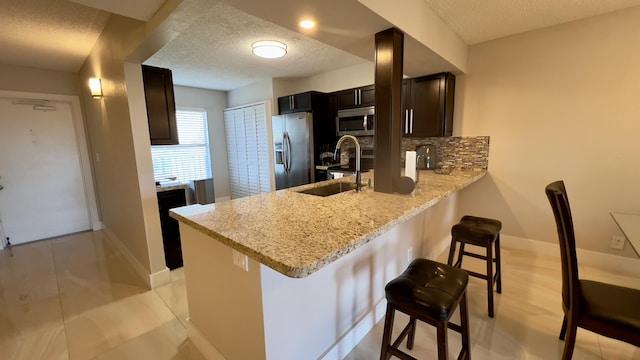 kitchen featuring a kitchen bar, appliances with stainless steel finishes, backsplash, a textured ceiling, and sink