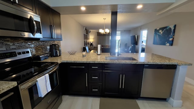 kitchen with sink, stainless steel appliances, a notable chandelier, pendant lighting, and decorative backsplash