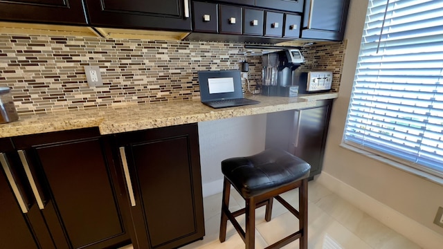 bar featuring dark brown cabinetry, decorative backsplash, light tile patterned flooring, and light stone countertops