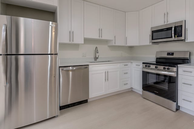 kitchen with stainless steel appliances, white cabinetry, light hardwood / wood-style floors, and sink