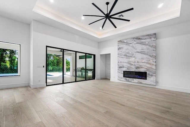 unfurnished living room with ceiling fan, light hardwood / wood-style flooring, a fireplace, and a tray ceiling