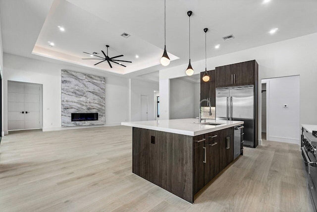 kitchen featuring a tray ceiling, sink, a fireplace, hanging light fixtures, and an island with sink