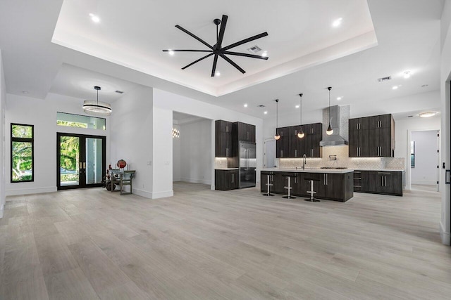 living room with ceiling fan with notable chandelier, a tray ceiling, light hardwood / wood-style flooring, and sink