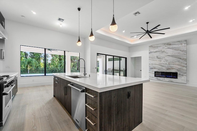 kitchen with ceiling fan, sink, a premium fireplace, a center island with sink, and appliances with stainless steel finishes