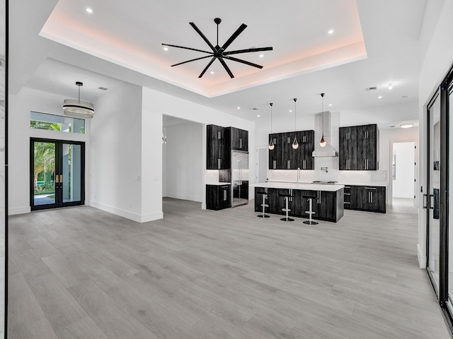 living room featuring a tray ceiling, french doors, light hardwood / wood-style floors, and ceiling fan with notable chandelier