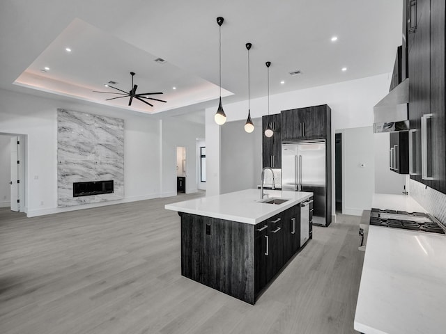 kitchen featuring pendant lighting, sink, a raised ceiling, and an island with sink