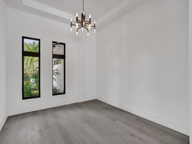 unfurnished room featuring a chandelier, hardwood / wood-style floors, and a raised ceiling