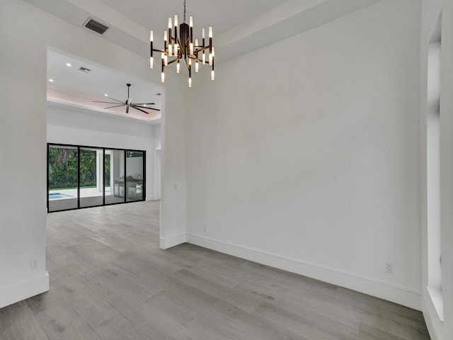 empty room with ceiling fan with notable chandelier, light wood-type flooring, and a tray ceiling