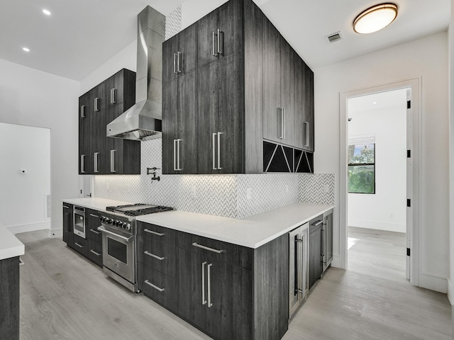 kitchen with light hardwood / wood-style floors, wall chimney range hood, stainless steel stove, and tasteful backsplash