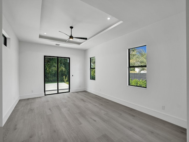 unfurnished room featuring a raised ceiling, a wealth of natural light, ceiling fan, and light hardwood / wood-style floors