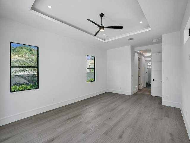 spare room with light wood-type flooring, a tray ceiling, and ceiling fan