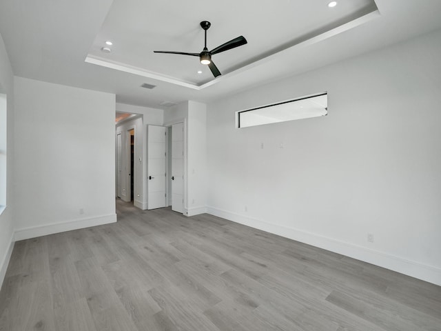 spare room featuring a raised ceiling, ceiling fan, and light hardwood / wood-style floors