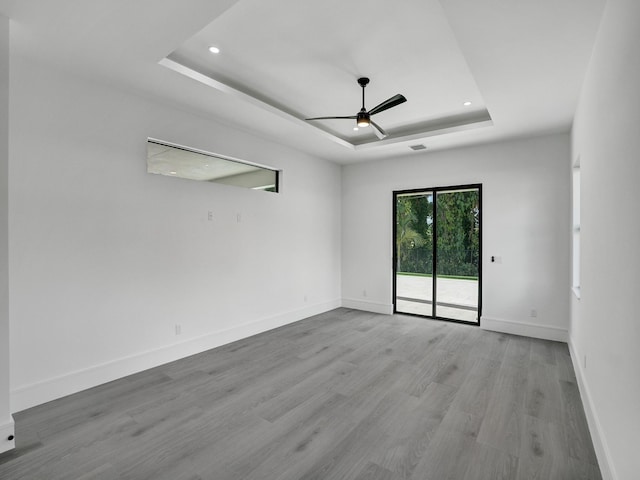 empty room with light wood-type flooring, a tray ceiling, and ceiling fan