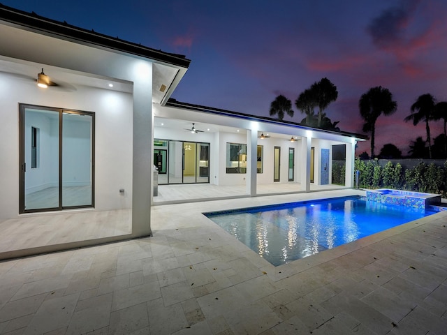 pool at dusk with ceiling fan, a patio area, and an in ground hot tub