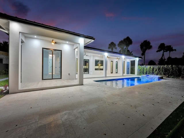 pool at dusk with a patio and a hot tub