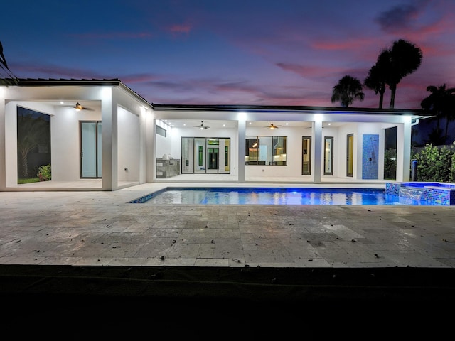 pool at dusk featuring an in ground hot tub, ceiling fan, and a patio area