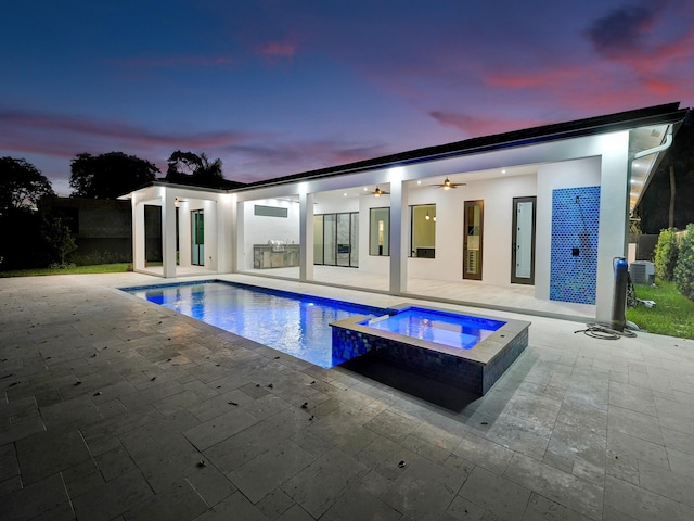 pool at dusk with ceiling fan, a patio area, and an in ground hot tub