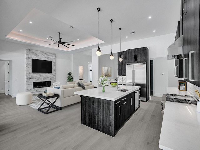 kitchen with hanging light fixtures, a raised ceiling, a kitchen island with sink, and sink