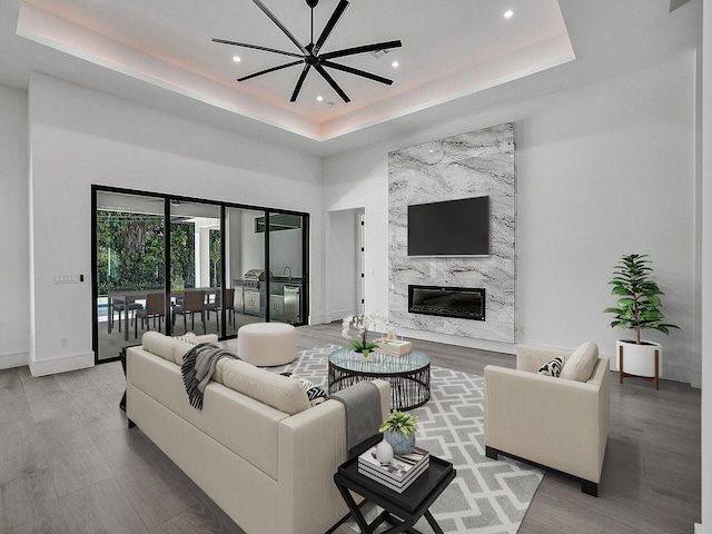 living room featuring wood-type flooring, a raised ceiling, ceiling fan, and a premium fireplace