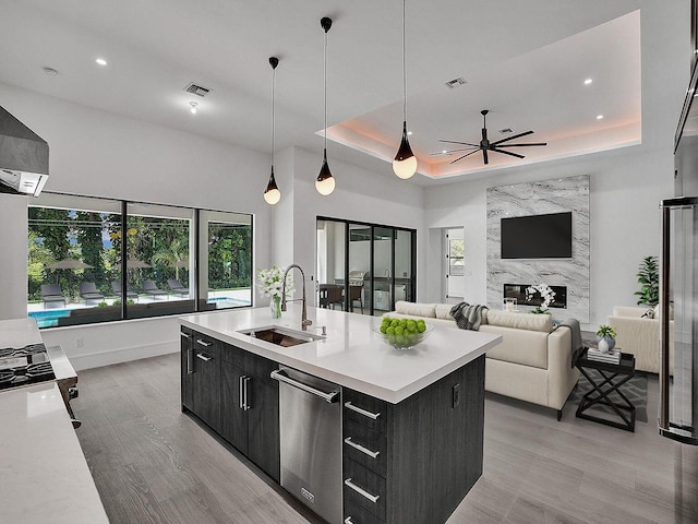 kitchen with sink, stainless steel dishwasher, ceiling fan, an island with sink, and a tray ceiling