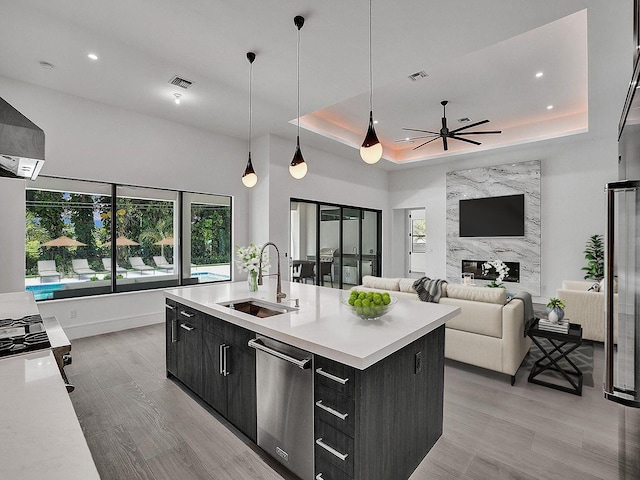 kitchen with ceiling fan, sink, a raised ceiling, decorative light fixtures, and a center island with sink