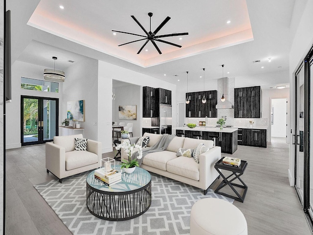 living room with a raised ceiling, light hardwood / wood-style flooring, and ceiling fan with notable chandelier