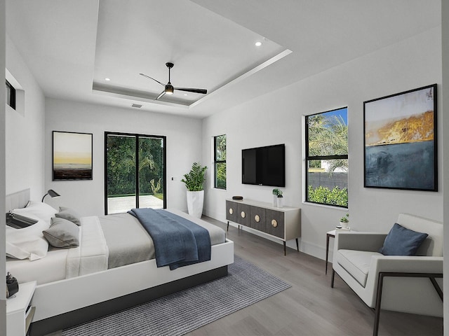 bedroom with access to exterior, light hardwood / wood-style floors, a raised ceiling, and ceiling fan