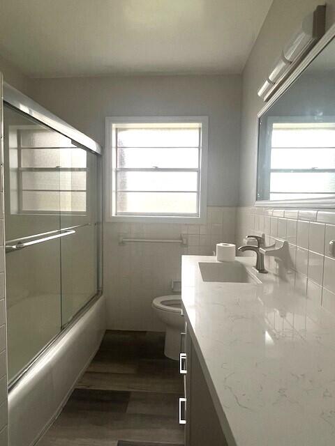 full bathroom with enclosed tub / shower combo, wood-type flooring, toilet, vanity, and tile walls