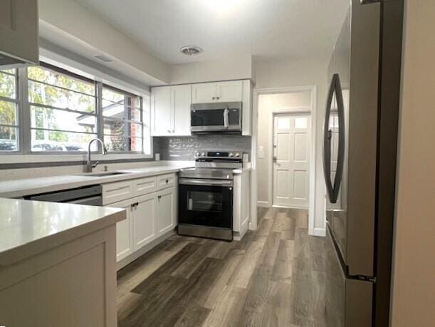 kitchen with sink, dark hardwood / wood-style floors, appliances with stainless steel finishes, tasteful backsplash, and white cabinetry