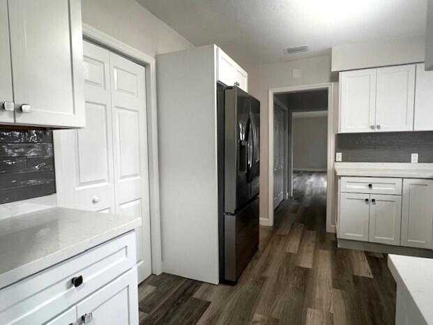 kitchen featuring dark hardwood / wood-style floors, black fridge with ice dispenser, white cabinetry, and decorative backsplash